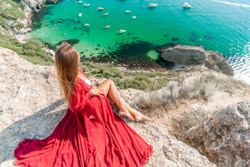 Woman red dress sea. Happy woman in a red dress and white bikini sitting on a rocky outcrop, gazing out at the sea with boats and yachts in the background.