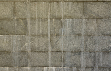 The texture of a wall of large granite tiles that are covered with white streaks when exposed to...