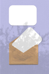 An envelope with two sheets of white paper on violet background. Mock up with an overlay of tropical tree foliage shadows. Natural light casts shadows from the leaves of a tree branch. Vertical