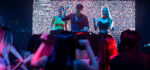 DJ with Turntables at nightclub. Group of diverse young people dancing in night club. Nightlife and...