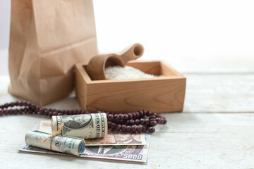 Fototapeta na wymiar Rice in a wooden box and money placed on a wooden table ready for donation, ZAKAT donation, Muslim tradition concept