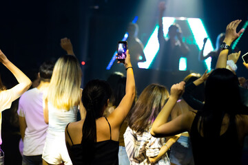 Audience Captures the show with smartphone. music concert live on stage. diverse young people dancing in night club. Nightlife and disco dance party concept. Fun music festival