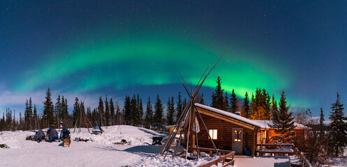 Panorama of Aurora Borealis, Northern Lights, over aboriginal wooden cabin at Yellowknife,...