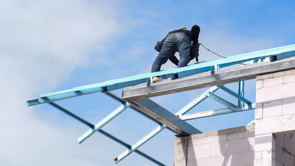 Workers are installing gray roof tiles wearing seat belts to ensure safe working at heights.