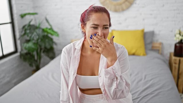 Exhausted young redhead woman caught mid-yawn sitting comfortably in bed, expressing the cozy morning struggle to wake up in her pleasantly relaxed bedroom interior.