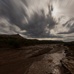 Bright moonlight lights the clouds above the Southern Utah desert near Gooseberry Mesa after a nighttime summer rain storm. Some rain remains along the bottom of the sandy arroyo.