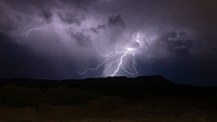 Threads of lightning spread out from the dark purple storm clouds above Gooseberry Mesa in Southern...
