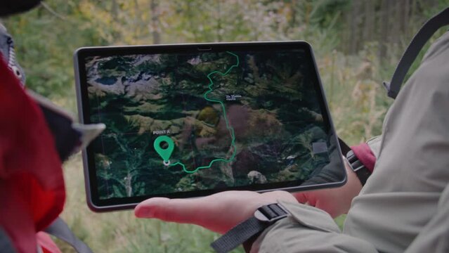 Close up shot of hiker holding digital tablet computer in hand. Tablet with displayed map and trail way in mountains. Tourists stopped to check route. Nature discovery and outdoor exploration concept.