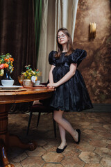 Obraz na płótnie Canvas Elegant girl in black dress standing by a table with flowers