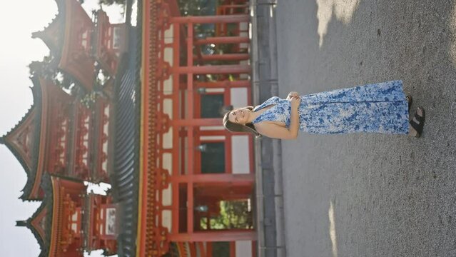 Beautiful hispanic woman confidently standing, enjoying and smiling while looking around the traditional heian jingu shrine, kyoto, japan