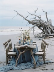 Obraz premium Outdoor dining scene on a sandy beach with elegant table setup and driftwood backdrop