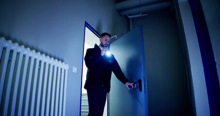 Mature Male Security Guard With Flashlight Standing In Corridor