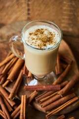A cup of coffee with cinnamon stands on a wooden board. Scattered cinnamon sticks on the background