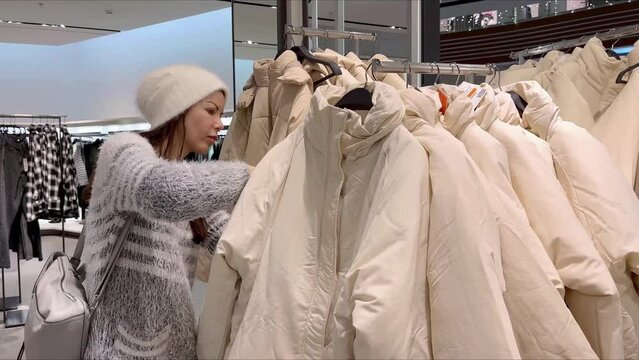 Among a large selection of clothes, hang on hangers on a rack-hanger, correctly placed, hung by colors and sizes, the buyer chooses and looks after the clothes of the buyer. Buying clothes in a store