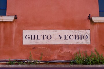 Old town of Italian City of Venice with red facade and street name sign at Ghetto Vechio on a sunny...