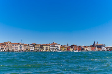 Obraz premium Old town of Italian City of Venice with colorful facades of historic houses and church tower seen from Canale san Giorgio on a sunny summer day. Photo taken August 7th, 2023, Venice, Italy.