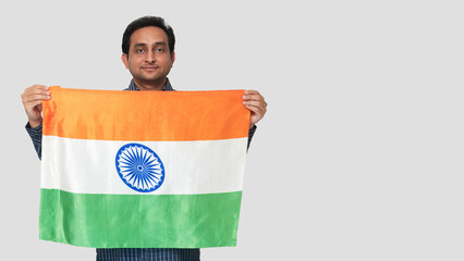Young Indian man holding the Indian flag, showing pride to be Indian, on the festival of 26 January, isolated white background.
