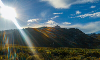 sunshine rays shining out behind mountains and blue skies. Light refraction. Rainbow sun rays. sunlight.