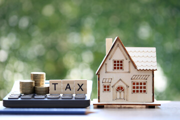 Tax concept,Model house with stack of coins money and tax word on green background,Business investment and Property tax concept
