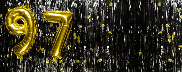 Gold foil balloon number number 97 on a background of black tinsel decoration. Birthday greeting...