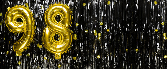 Gold foil balloon number number 98 on a background of black tinsel decoration. Birthday greeting...