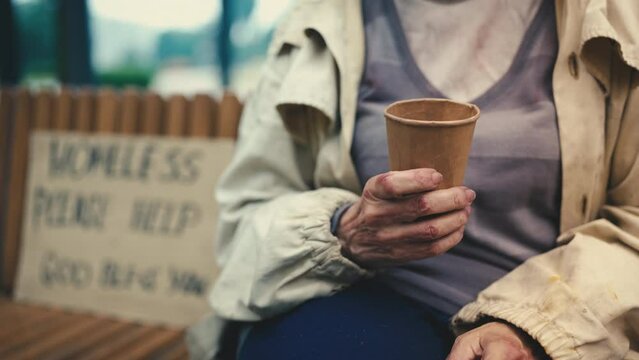 Homeless aged woman holding out paper cup, asking for spare change on the street