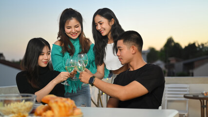 Group of cheerful people having fun while toasting with alcohol on a rooftop party