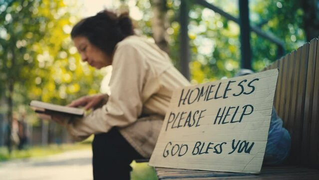 Homeless cardboard sign on bench, senior woman refugee reading a book nearby