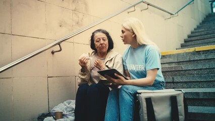 Volunteer fills out charity form on tablet while homeless woman eats a sandwich