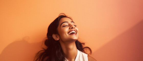 Fototapeta premium Portrait of a beautiful young indian woman laughing against orange wall