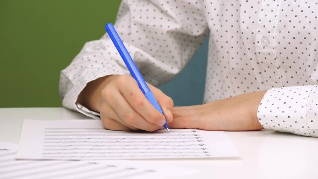 A child writes with a pen while sitting at a desk with a speckled plan. A schoolboy studying notes, music school, music children