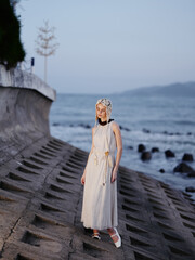 Sunny Beach Beauty: A Pretty, Attractive Female Model Standing on the Coast, Enjoying a Relaxing Summer Day in a Blue Dress, with White Hair Blowing in the Wind, Against a Background of Clear Blue Sky