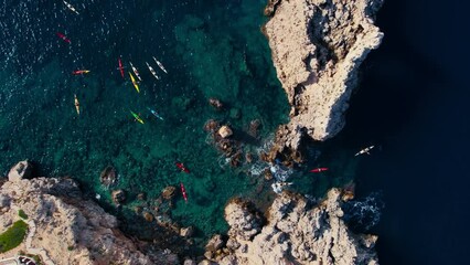 Aerial shot of kayak group tour exploring coastline of Mallorca, Spain. Drone view of kayakers paddle over coral reef and turquoise clear blue water. Fun sport activity for family on vacation