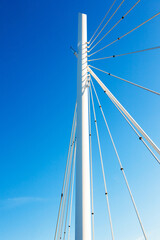 White vertical pillar of a bridge with steel braces, against a background of blue sky, view from below.