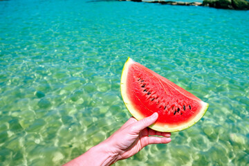 relaxation composition. male hand with a piece of ripe watermelon against the background of the blue sea, vacation concept