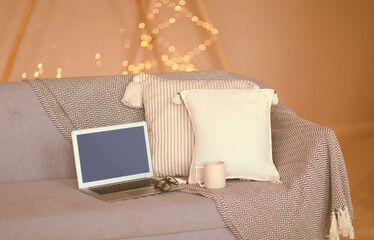 Laptop on sofa in room with festive lights