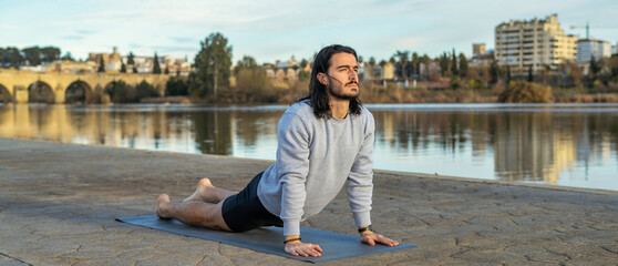 Male Doing Cobra Pose During Yoga Training Next To A River That Crosses The City