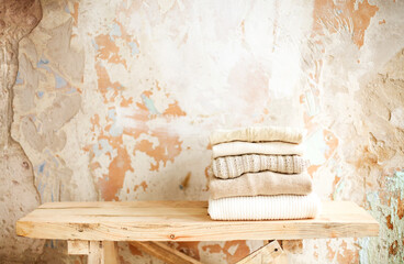 Stack of neatly folded clothes lies on raw wooden shelf against beige color grunge concrete