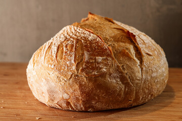 Fresh home made bread on the kitchen wood counter top. Close up photo with a delicious sourdough bread got out of the oven. Bake bread at home.