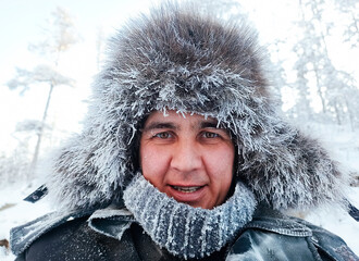 close-up portrait of a smiling Caucasian middle-aged man in a winter fur hat in the forest and with...