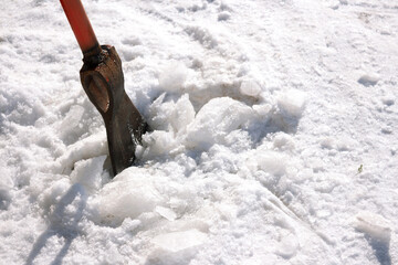 human clears the yard from the ice with a sharp orange-colored iron cleaver, on a bright sunny...