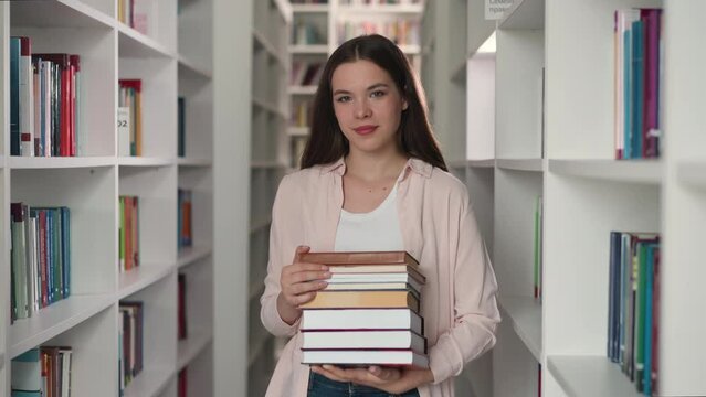 Young teacher with folio stack in college library. Happy librarian recommends literature for reading in bookstore. Pretty lady with books collection