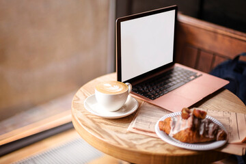 Freelance workplace in coffee shop. Laptop, newspaper and morning breakfast on table