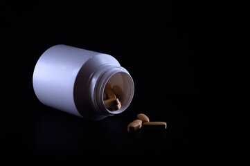 Medication bottle and spilled brown capsules on black background isolated. Medical concept. Vitamins and supplements. 