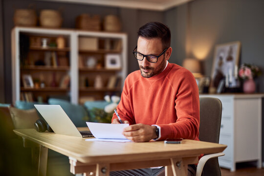 Businessman working from home in an orange sweater. He is signing some documents. - Powered by Adobe