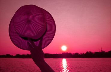 Surreal pop art of French rose colored hand holding straw hat waving to to sunset sky