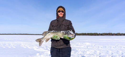 Man Holding a Fish pike in Hands. Winter fishing. Banner, copy space