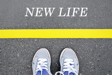 there are sneakers on the light asphalt with a yellow stripe and the inscription new life, top view, creative concept