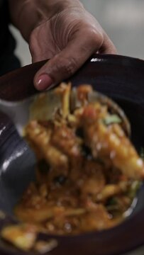 A close-up of a female hand serving freshly cooked fish curry onto a plate