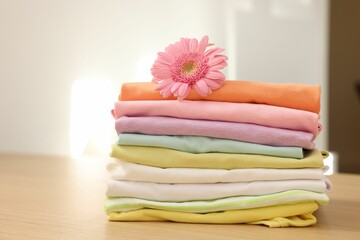 Stack of clean clothes and pink flower on wooden table